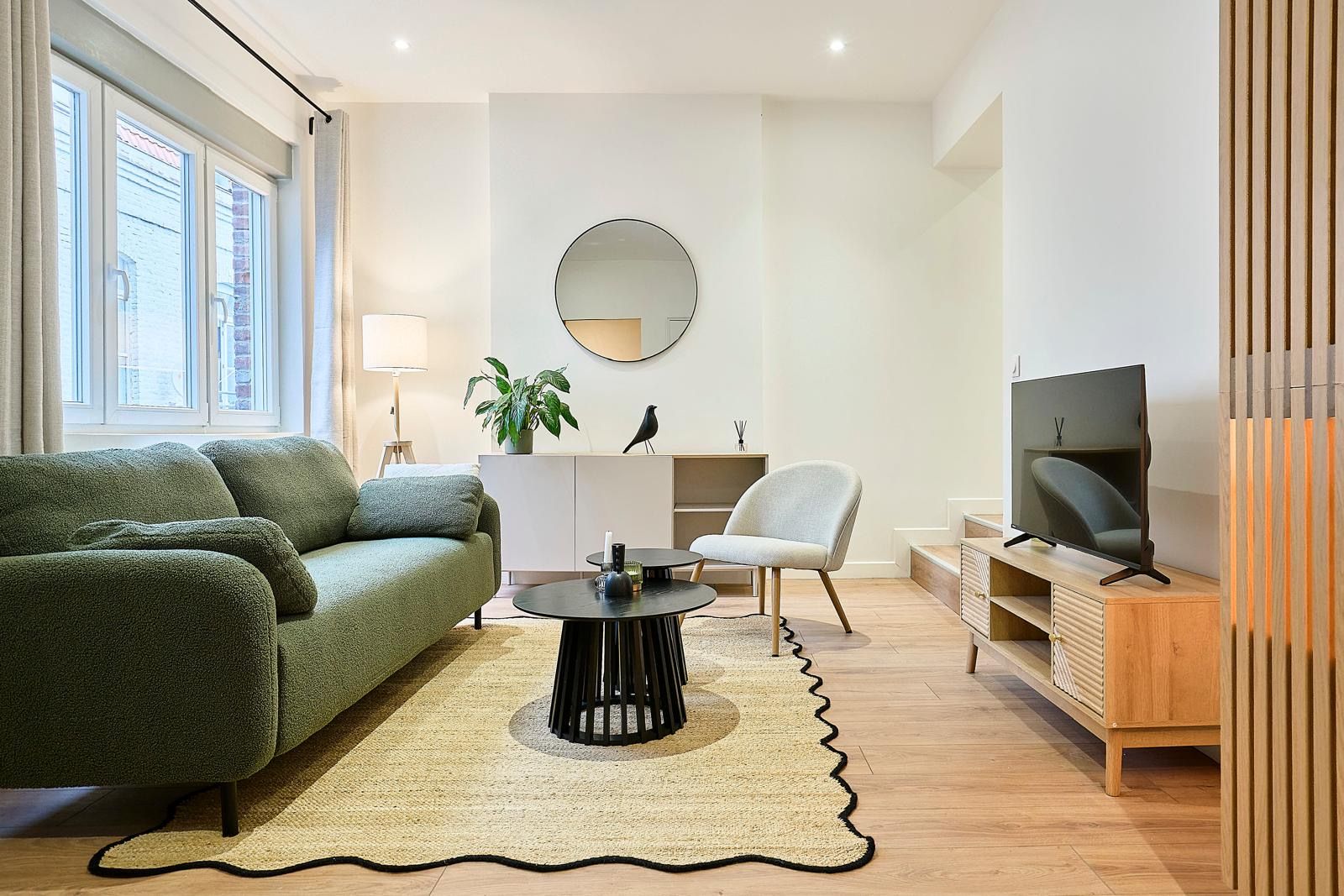 Séjour avec canapé vert, tapis en jute et meuble TV en bois